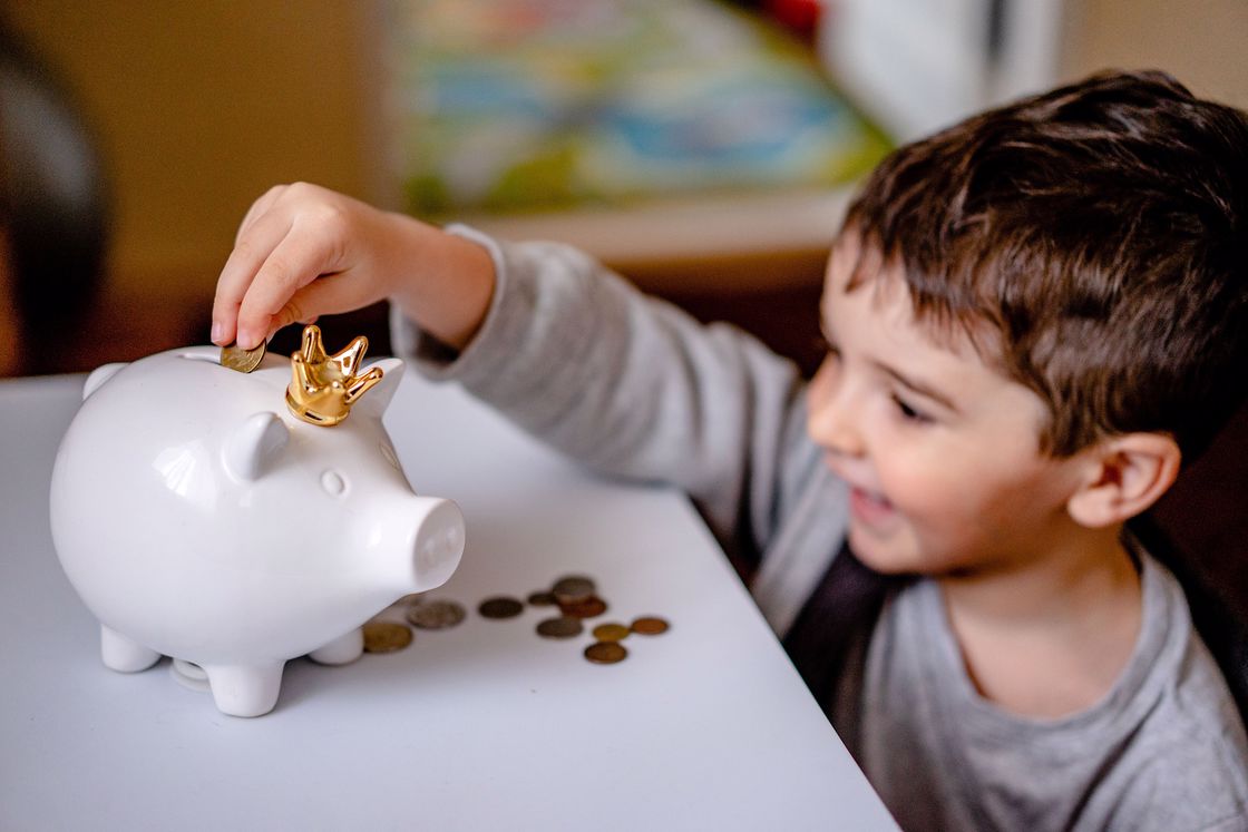 Little boy putting coins in a white piggy bank