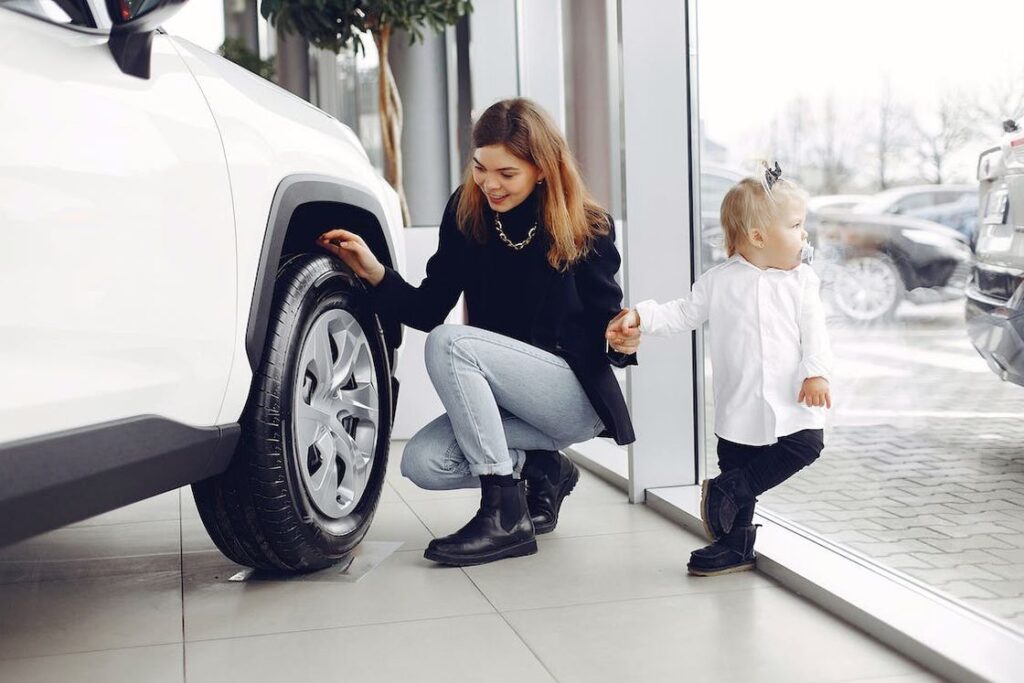 Woman with daughter checking the car wheel of a white car in a showroom