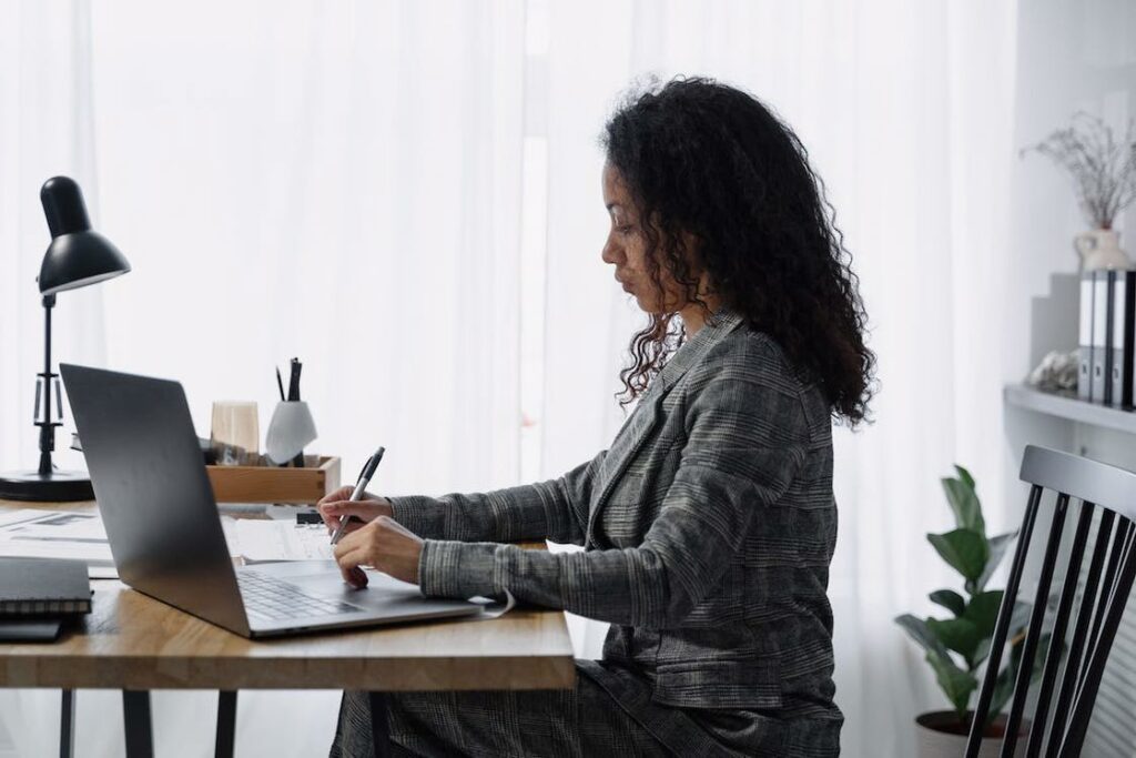 Woman using her laptop, while her other hand is writing notes on a pad paper