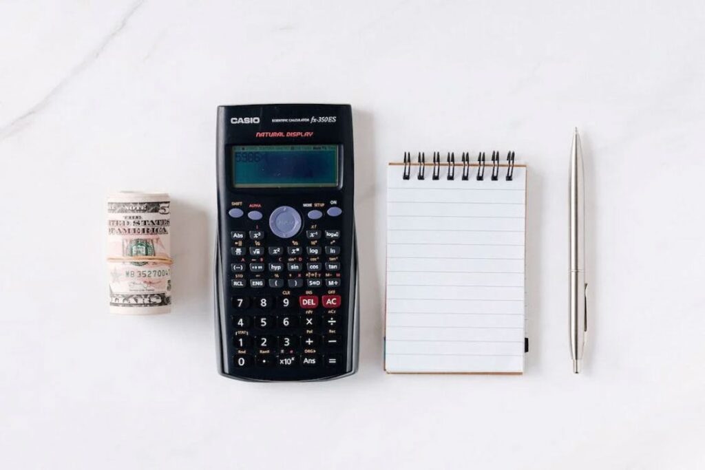 Rolled up paper bills, calculator, notepad and pen on a white table