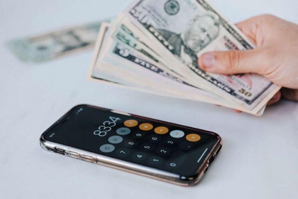 Person holding cash while a calculator app is opened on a smartphone