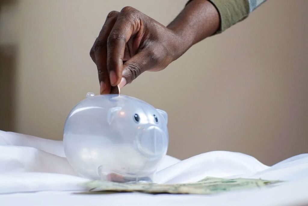 Person putting a coin in a transparent piggy bank