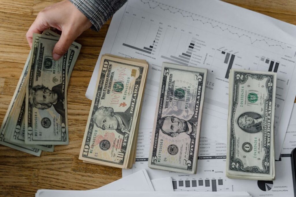 Person stacking dollar bills into 4 columns on top of data sheets on a table