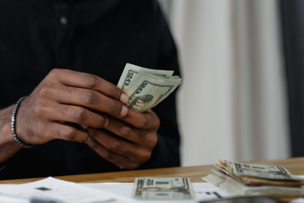 A person in black long sleeves counting US dollar bills placed on a brown table