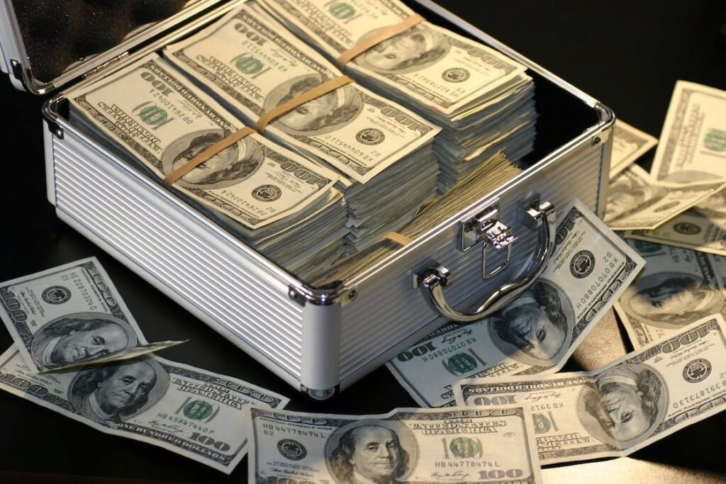 Stacks of dollar bills placed on a gray metal case while loose bills are scattered around it