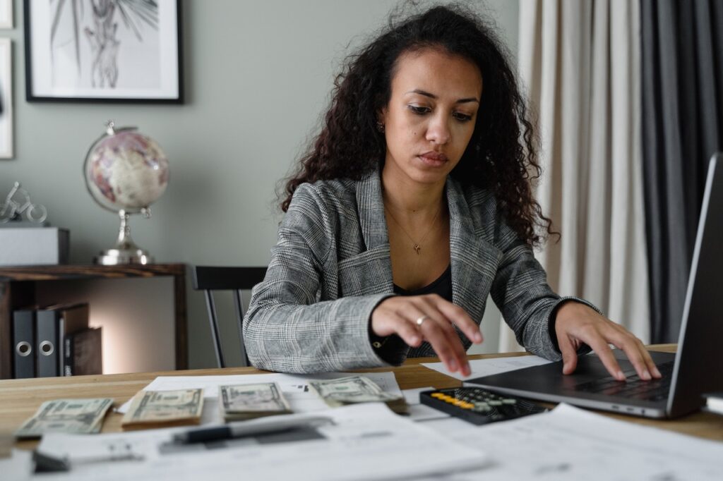 A woman in a plaid blazer using a silver laptop and smartphone on budgeting