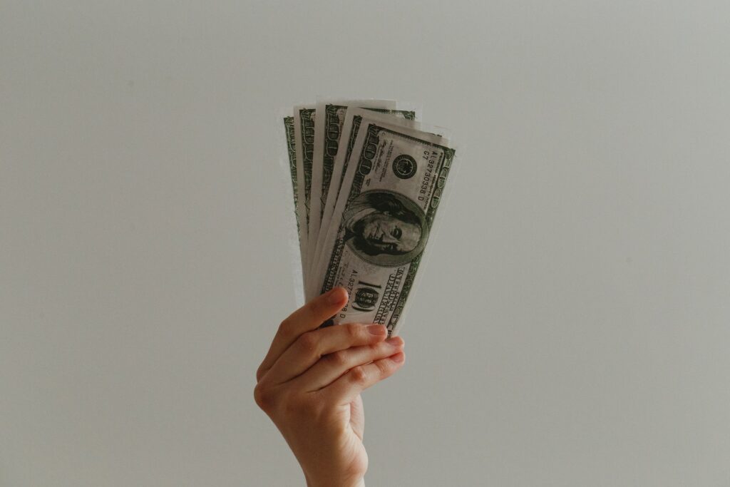A person holding US dollar bills on a gray background