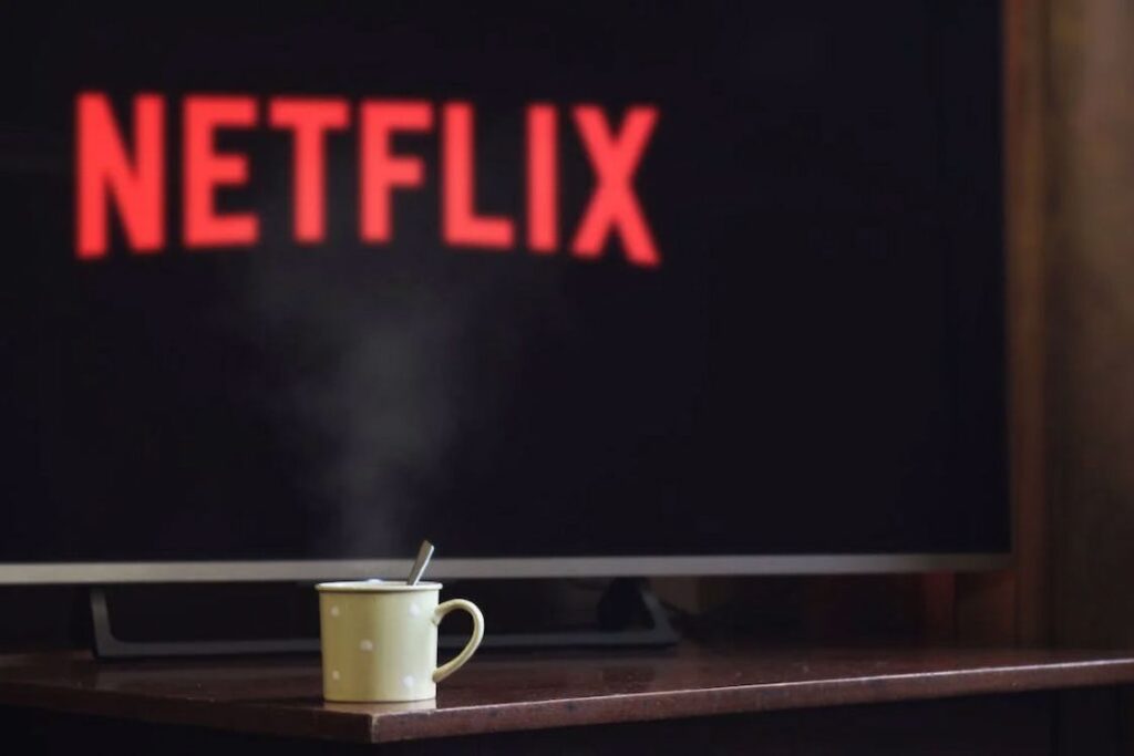 Steaming cup of coffee placed in front of the TV that has the Netflix logo in its screen