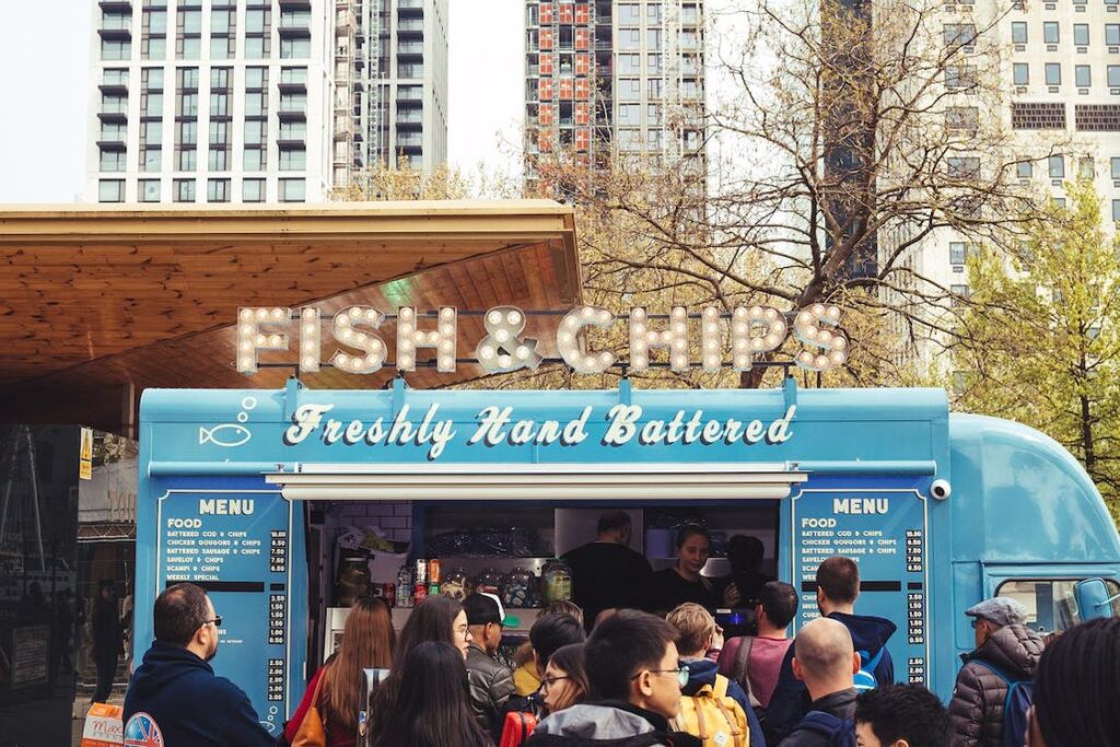People crowding around a Fish and Chips food truck in a park