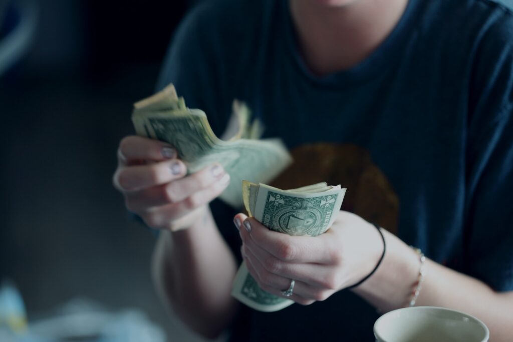 A woman in a blue t-shirt counting US dollar bills while seated in the living room