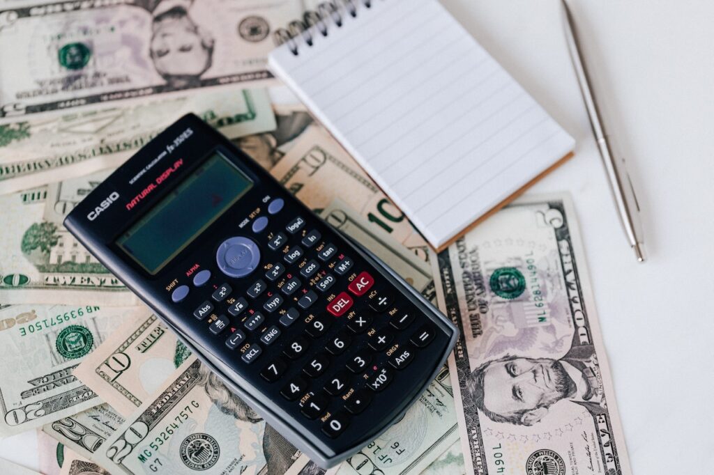 A scientific calculator, notebook, and US dollar bills were placed on a white surface