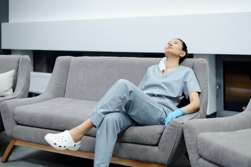 A nurse wearing a scrub suit resting on a gray couch