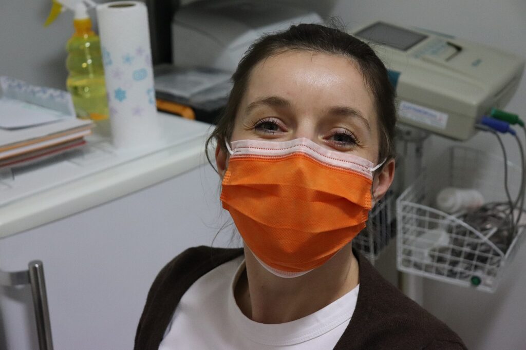 A nurse wearing a black cardigan on top of a white scrub suit and an orange face mask inside the hospital