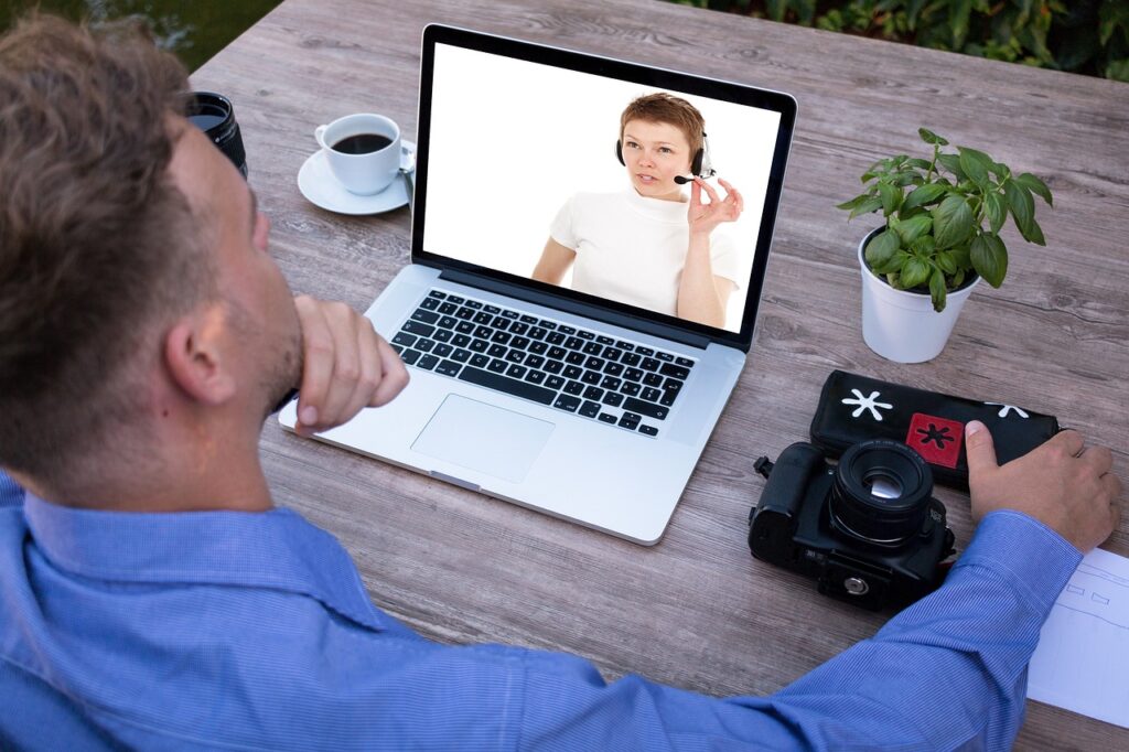 A man in front of a laptop watching a woman with headphones speaking in its microphone
