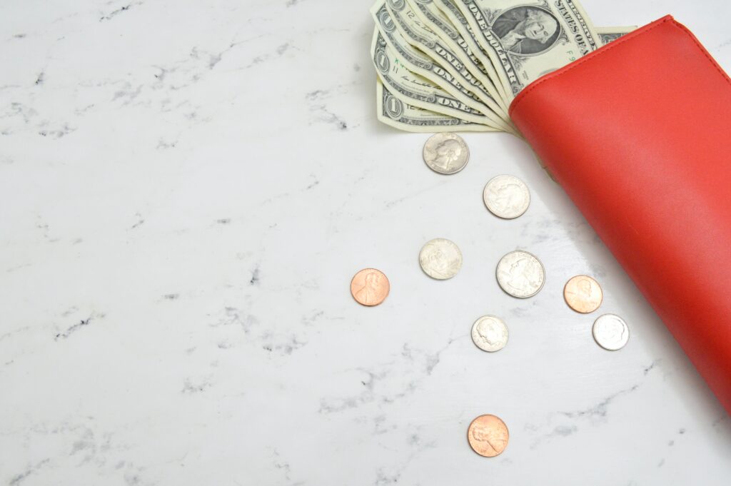 A red wallet with dollars beside some coins laying on a marbled tile