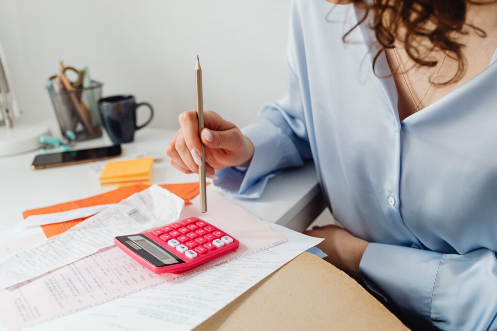 A woman pressing a pink calculator using a pencil with some receipts in front of her
