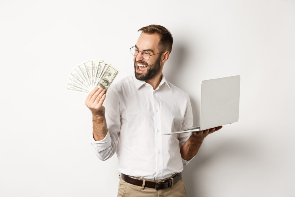 A man holding a dollar bill on his left arm and a laptop on his right arm