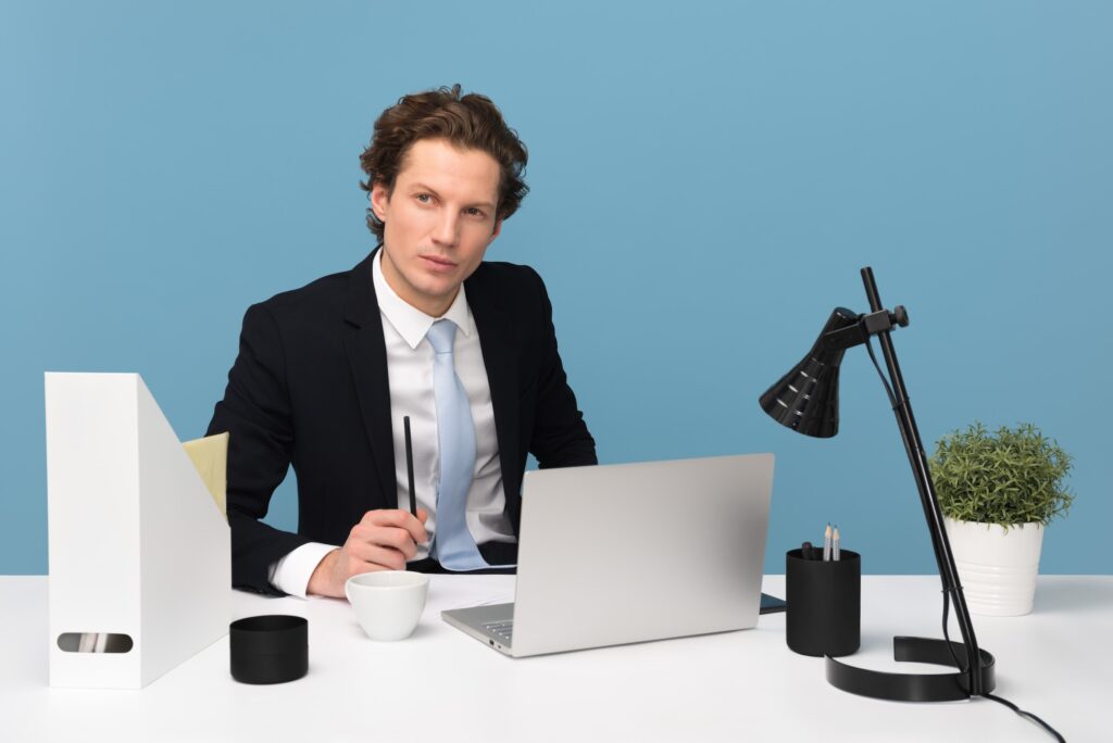 A man in suit thinking in front of a table with laptop and office equipments