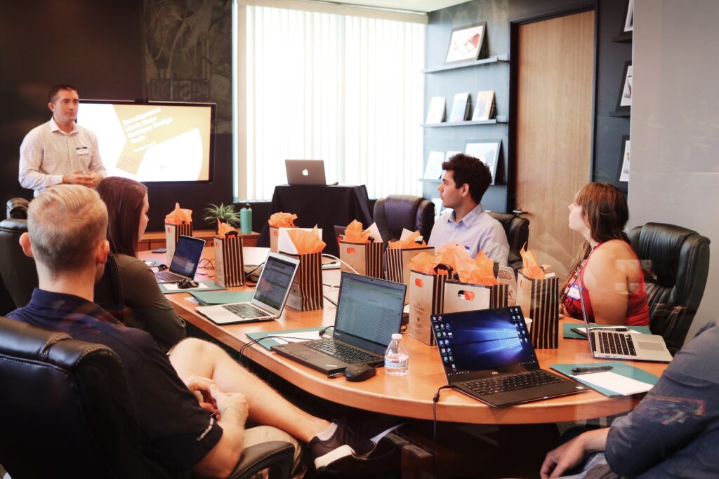 A group of six people in a meeting room with laptops sitting on chairs