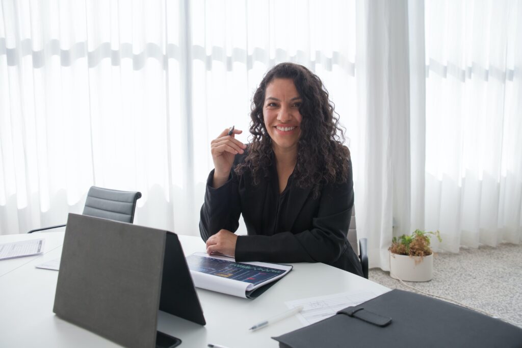 A woman smiling while holding a pen and with a business report in front of her