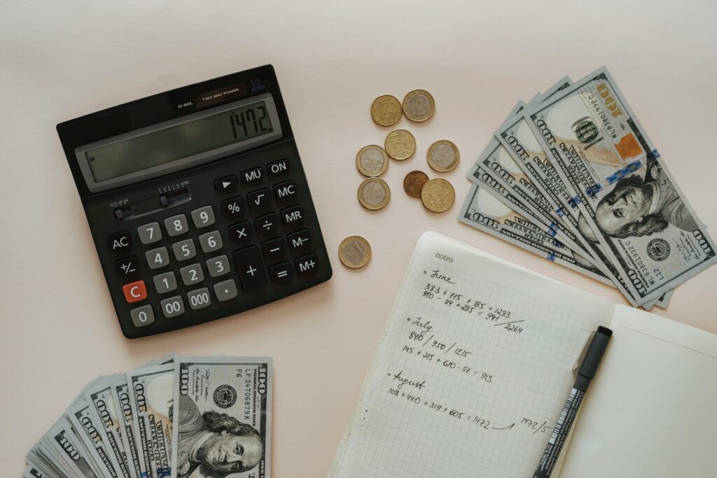 A calculator, some dollar bills. coins, and computation written on a notebook