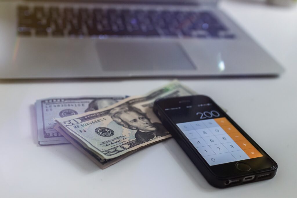 An image of a laptop, a cellphone, and some dollar bills