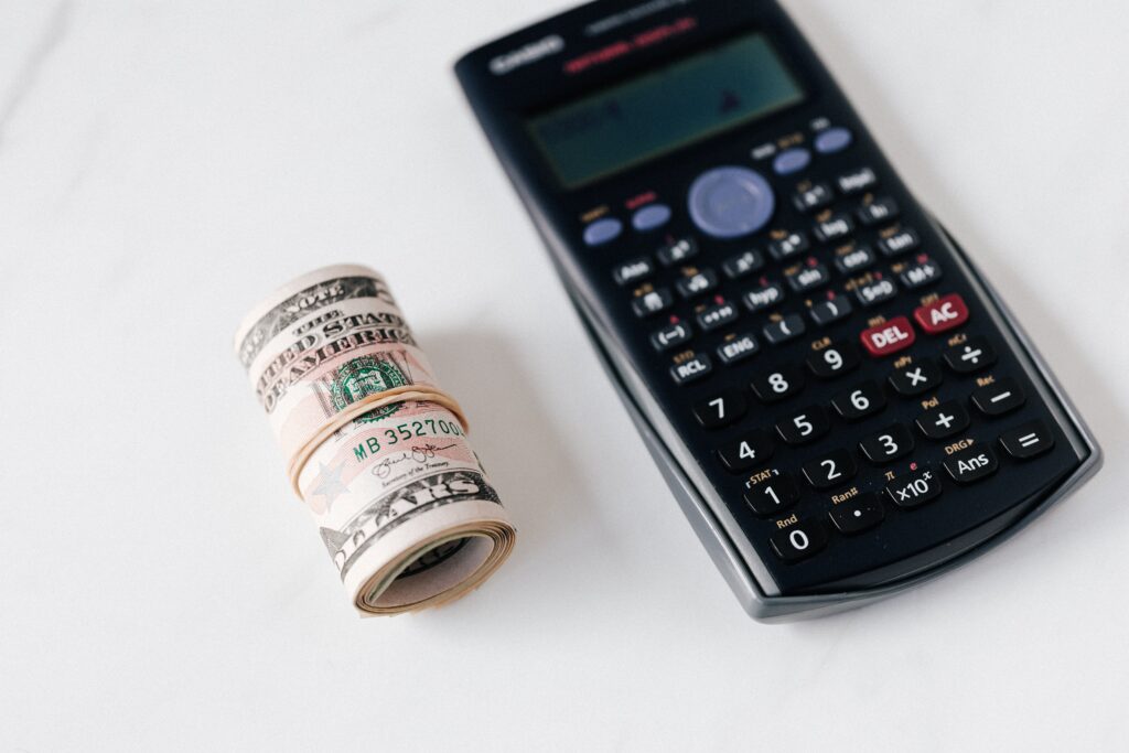 A rolled dollar bills and a calculator beside it