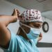 A nurse wearing a white and red polka dots head wrap, blue surgical mask, and blue scrubs inside the hospital